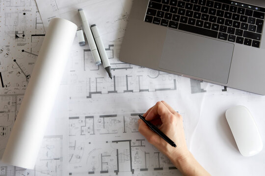 Architect working on blueprints at office desk with laptop