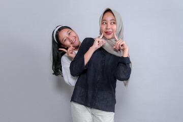 Two young Asian women posing playfully with cute finger gestures and joyful expressions. One peeks...