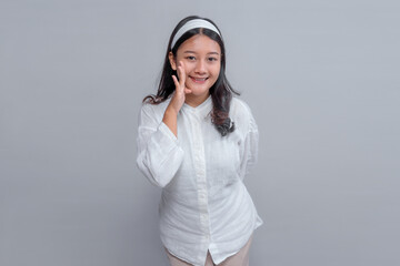 Portrait of a young Asian woman in white shirt smiling and making a speaking gesture with her hand...