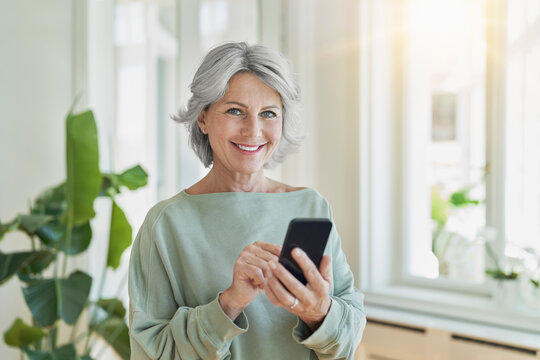 Smiling woman using mobile phone in a bright living room