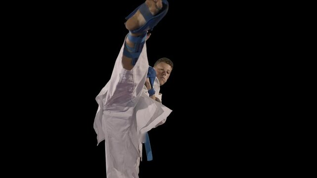 Young male blue belt karate fighter does high kick on black background