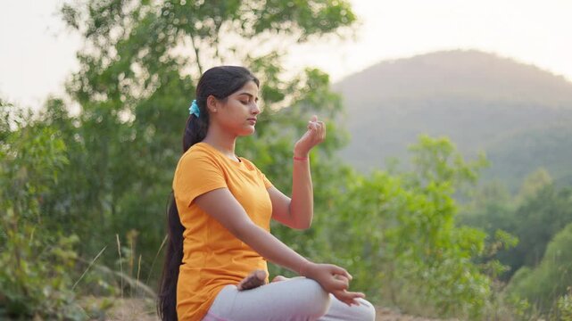 Fit young woman sitting in lotus position practicing anulom vilom pranayama against mountain landscape.