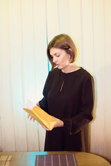 A woman looks down into a yellow paper bag she is holding indoors. She has short brown hair and is...