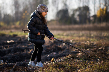 Young girl exploring nature holding stick in field