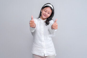 Young Asian woman in a white shirt and headband, smiling with her eyes closed while showing a double thumbs up gesture, expressing joy, satisfaction, and positive approval in studio setting.
