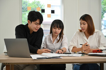 Fototapeta premium Three young professionals working together on a project, discussing design plans and strategies around a laptop in a bright, modern office