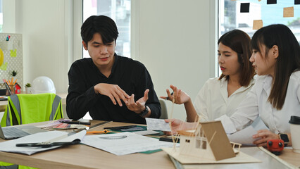 Professional design team having a focused discussion on construction plans and design solutions, surrounded by models and technical documents