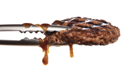 Juicy burger patty held in tongs, dripping with grilled fat, sizzling on white backdrop
