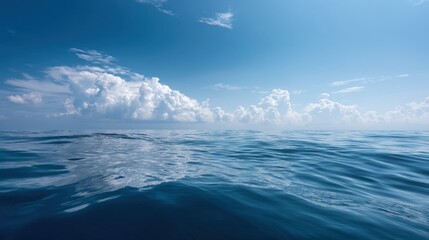 Fototapeta premium Serene calm ocean under bright blue sky with scattered white clouds and gentle waves.