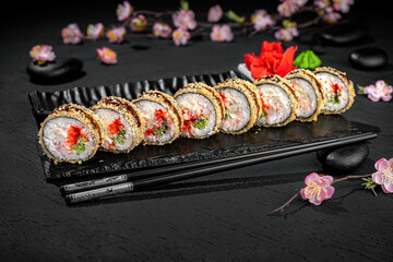 Elegant sushi roll tempura presented lengthwise on a textured black background with a delicate blooming sakura branch in the background. Minimalist and artistic Japanese food presentation.