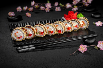 Elegant sushi roll tempura presented lengthwise on a textured black background with a delicate blooming sakura branch in the background. Minimalist and artistic Japanese food presentation.
