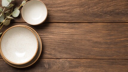 A serene display of two ceramic bowls on a rustic wooden table with eucalyptus leaves nearby