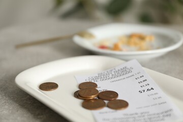 Tips, receipt and dirty plate on grey table in cafe, closeup