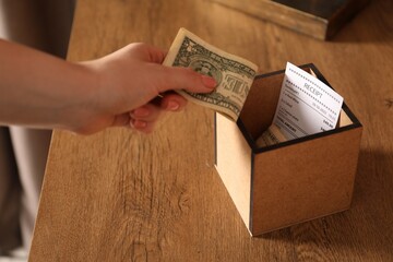 Woman putting tips into box at wooden table indoors, closeup
