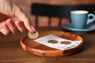 Woman putting tips onto plate at wooden table in cafe, closeup