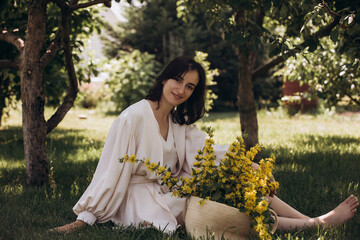 Portrait of a young adult beautiful brunette woman in a garden with yellow flowers