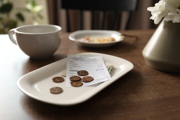 Tips, receipt, dirty plate and cup on wooden table in cafe, closeup