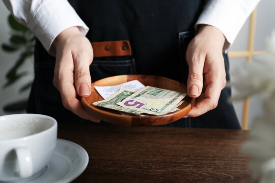 Waitress holding tips and receipt at wooden table in cafe, closeup
