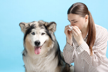 Woman suffering from allergy with her dog on light blue background