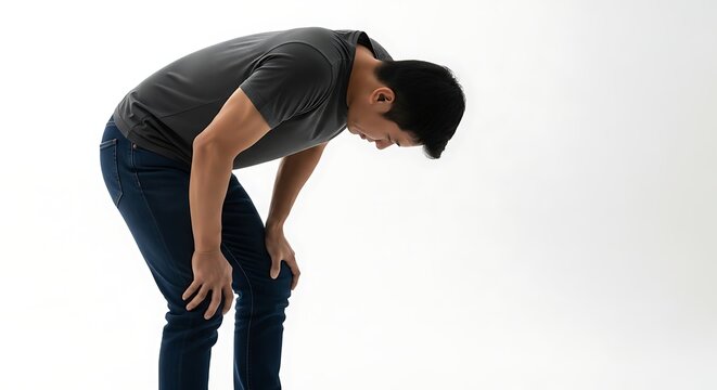 Man in gray shirt and jeans bending over with hands on knees against white wall