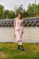 Woman in a rose dress stands before a brick wall in the summer