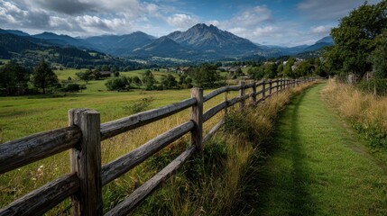 Fototapeta premium Scenic mountain landscape with a meadow trail and wooden fence near a small village in the early afternoon light