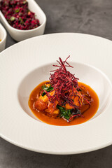 Shrimp in tomato sauce topped with crispy beet garnish and leafy greens