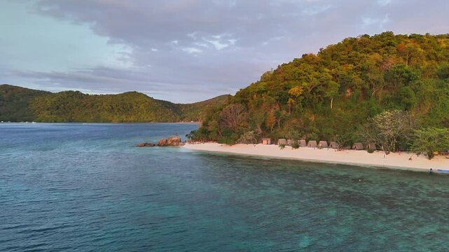 Secluded white sand beach lined with native huts and tropical trees, nestled on New Culaylayan Island, surrounded by clear turquoise waters near Linapacan Tourists Camp in the Philippines
