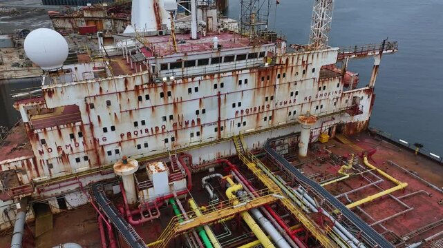 Aerial drone view of an old red tanker with a heavily rusted superstructure. The aging vessel is docked and prepared for dismantling into scrap metal at an industrial shipbreaking yard.