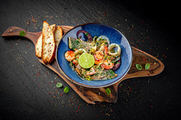 Luxury seafood salad with fish, shrimp, octopus, and mussels served with sauce on a dark background. Elegant gourmet dish.