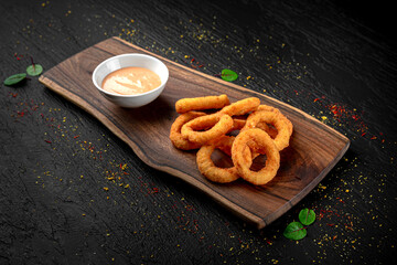 Golden fried onion rings or calamari served as a crispy appetizer on a dark background. Classic...