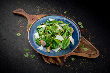 Fresh green spinach salad topped with parmesan cheese on a dark background. Healthy vegetarian dish with minimal presentation.