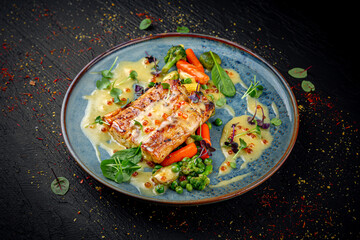 Baked salmon fillet served with a mix of vegetables on a dark background. Healthy gourmet dish.