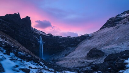 Obraz premium Majestic waterfall cascading down rocky mountain valley at sunrise, displaying vibrant pink and blue hues in the sky.