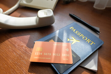 A blue passport cover with an airplane icon, two credit cards, a pen, and a telephone on a wooden...