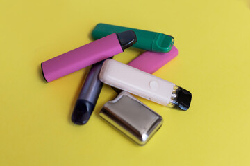 Colorful disposable vape devices on a yellow background, symbolizing unhealthy lifestyle choices, addiction, and modern smoking habits among youth. Concept of nicotine dependency and poor health