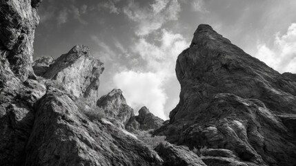 Dramatic black and white view of towering rocky mountains under cloudy sky.