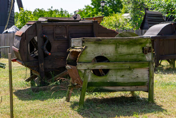 Weathered wooden threshing machines, partially broken and covered with moss, standing on grass in...