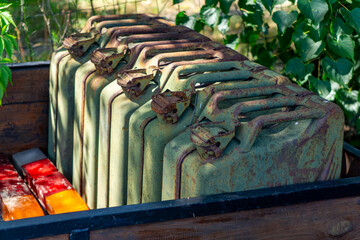 group of old, rusty military-style jerry cans placed in a wooden box, surrounded by green foliage....