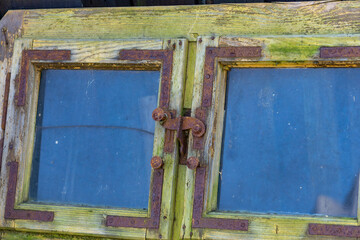 wooden window with blue glass panes and rusty metal fittings. The frame is weathered, with green patina and visible signs of aging. Rustic architectural detail, perfect for retro, countryside, or vint