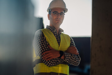 Confident construction engineer wearing hardhat and safety vest stands with crossed arms