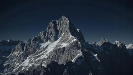 A dramatic view of snow capped mountain peaks against a dark blue night time sky landscape scene