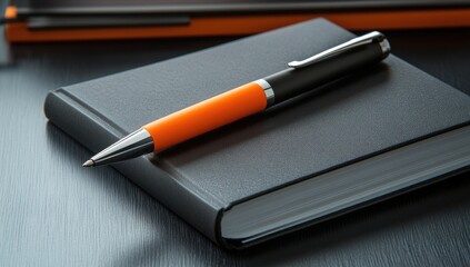 Dark gray notebook and orange pen on a dark surface
