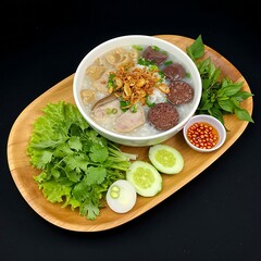 Vietnamese cháo lòng rice porridge with pork offal and blood pudding, garnished with fried shallots, arranged with fresh herbs like scallions and cilantro on A Teak Wood Platter
