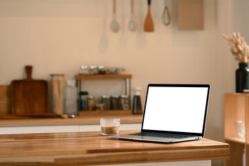 Laptop with empty screen and a cup of coffee placed on a wooden kitchen island
