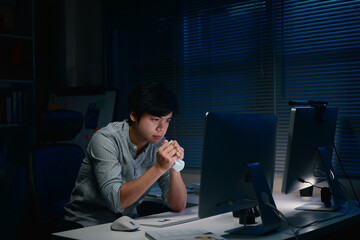 Tired man gripping a crumpled paper, sitting in the office and tackling important tasks after hours