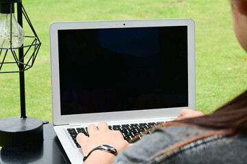 A woman is typing on a laptop in a park. The laptop screen is black, and the woman is focused on her work