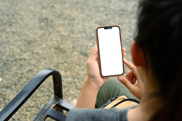 Over Shoulder view of woman sitting on a bench holding mobile phone with an empty display