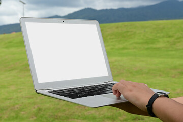 A person is holding a laptop in a grassy field. The laptop is open and the screen is blank