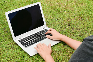 A person is typing on a laptop in a grassy field. The laptop is open and the screen is black